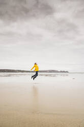 Young woman wearing yellow rain jacket at the beach, Bretagne, France - UUF19652