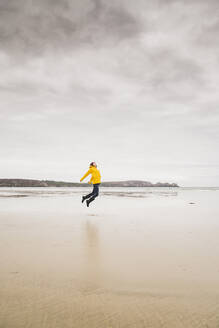 Junge Frau mit gelber Regenjacke am Strand, Bretagne, Frankreich - UUF19652