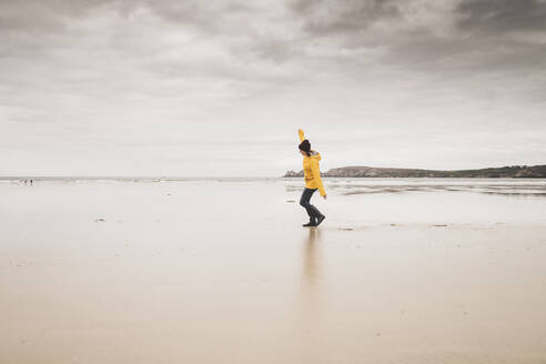 Junge Frau mit gelber Regenjacke am Strand, Bretagne, Frankreich - UUF19653