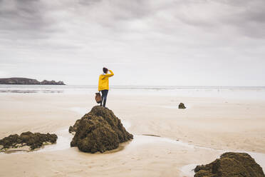 Junge Frau mit gelber Regenjacke am Strand, Bretagne, Frankreich - UUF19660