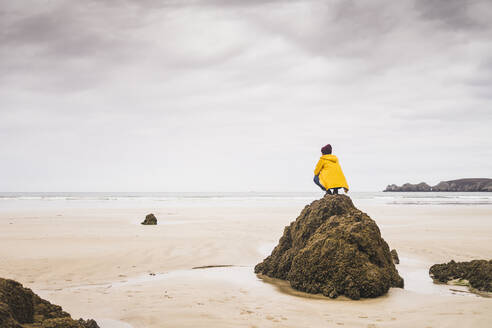 Young woman wearing yellow rain jacket at the beach, Bretagne, France - UUF19661