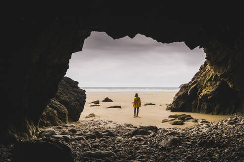 Young woman wearing yellow rain jacket at the beach at rock cave, Bretagne, France - UUF19665