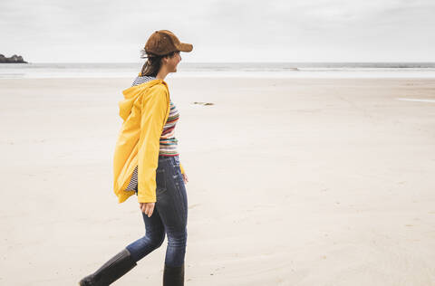 Junge Frau mit gelber Regenjacke am Strand, Bretagne, Frankreich, lizenzfreies Stockfoto