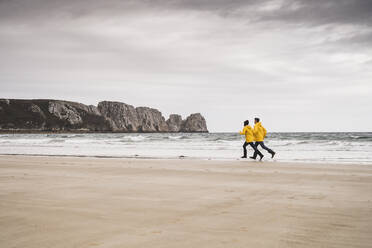 Junge Frau in gelben Regenjacken, die am Strand läuft, Bretagne, Frankreich - UUF19671
