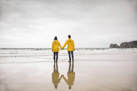 Junge Frau in gelben Regenjacken am Strand, Bretagne, Frankreich, lizenzfreies Stockfoto
