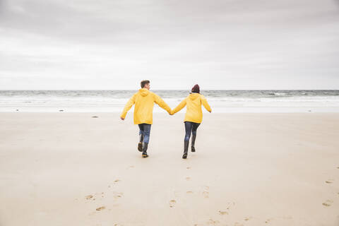 Young woman wearing yellow rain jackets and walking along the beach, Bretagne, France stock photo