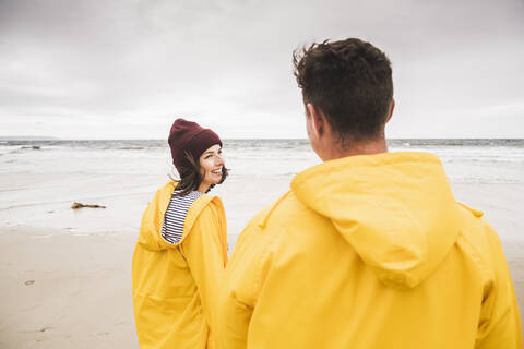 Junge Frau in gelben Regenjacken, die am Strand entlang läuft, Bretagne, Frankreich, lizenzfreies Stockfoto