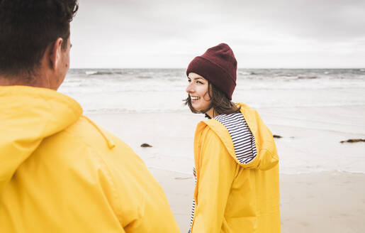 Young woman wearing yellow rain jackets and walking along the beach, Bretagne, France - UUF19690