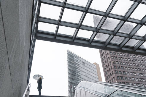 Mann mit Regenschirm telefoniert am Eingang des Bahnhofs Potsdamer Platz, Berlin, Deutschland - AHSF01146