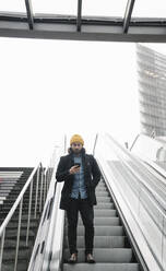 Mann steht auf Rolltreppe und schaut auf sein Smartphone, Berlin, Deutschland - AHSF01150