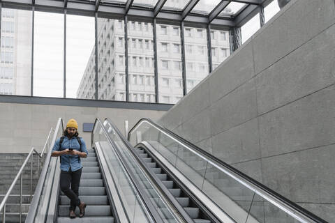 Mann auf Rolltreppe mit Smartphone, Berlin, Deutschland, lizenzfreies Stockfoto