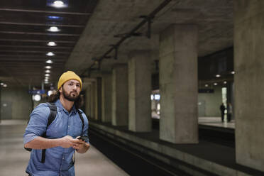 Porträt eines Mannes mit Smartphone, der am Bahnsteig wartet, Berlin, Deutschland - AHSF01157