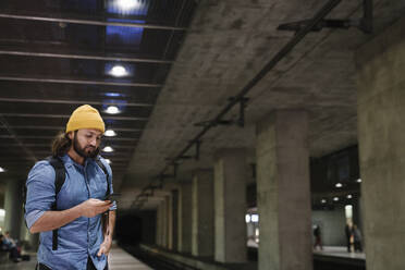 Mann wartet am Bahnsteig und benutzt sein Smartphone, Berlin, Deutschland - AHSF01158