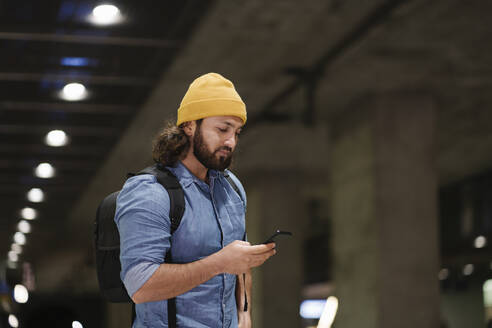 Mann mit Rucksack wartet am Bahnsteig und benutzt sein Smartphone, Berlin, Deutschland - AHSF01159