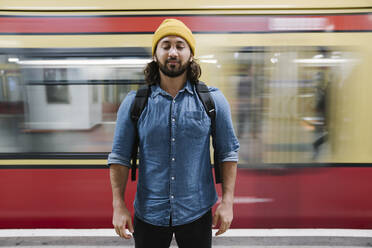Porträt eines bärtigen Mannes, der sich mit geschlossenen Augen am Bahnsteig entspannt, Berlin, Deutschland - AHSF01164