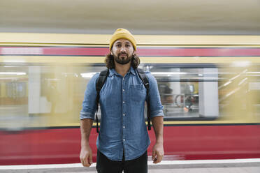 Porträt eines bärtigen Mannes, der am Bahnsteig vor einer fahrenden S-Bahn steht, Berlin, Deutschland - AHSF01165