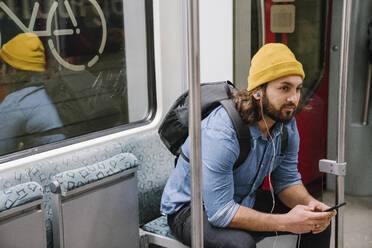 Mann mit Rucksack hört Musik mit Smartphone und Kopfhörern in der S-Bahn, Berlin, Deutschland - AHSF01169