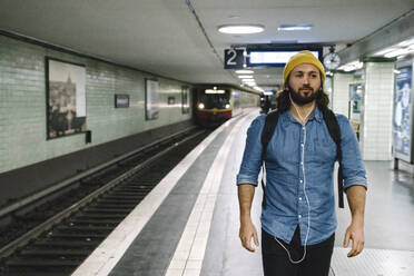 Porträt eines Mannes mit Rucksack und Kopfhörern auf einem Bahnsteig, Berlin, Deutschland - AHSF01170