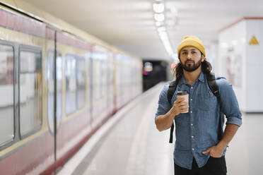 Porträt eines Mannes mit Rucksack und Kaffee zum Mitnehmen, der am Bahnsteig wartet, Berlin, Deutschland - AHSF01183