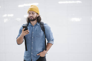 Porträt eines Mannes mit Rucksack, der auf sein Smartphone schaut - AHSF01185