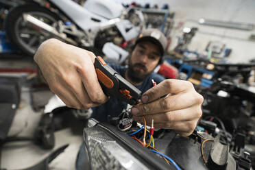 Mechaniker in einer Reparaturwerkstatt, der ein Motorrad repariert - MTBF00174