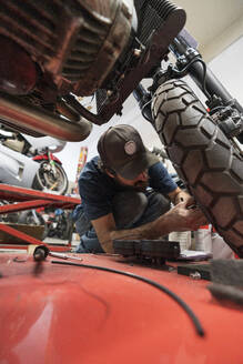 Mechaniker in einer Reparaturwerkstatt, der ein Motorrad repariert - MTBF00175
