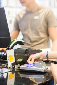 Hände einer Kundin beim Bezahlen mit Kreditkarte an der Kasse mit Kassiererin im Geschäft - MASF14335