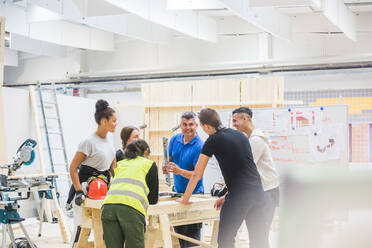 Male instructor teaching about level to trainees standing at workbench in illuminated workshop - MASF14356