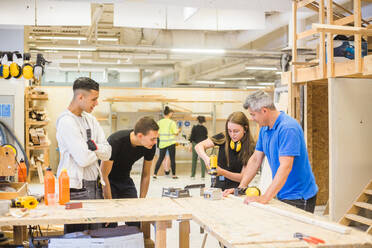 Male instructor and trainees watching while woman using power drill at workbench during training - MASF14388