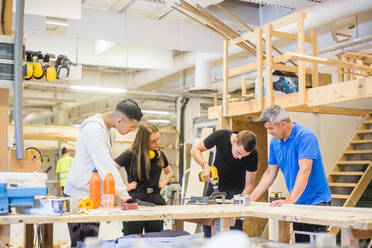 Carpenter and trainees watching while man using power drill at workbench during training - MASF14389