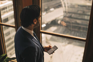 Hohe Winkel Ansicht der nachdenklichen Finanzberater Texting auf dem Handy durch Fenster im Büro - MASF14458