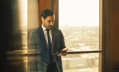 Mid adult legal professional using smart phone while standing against window at law office - MASF14461