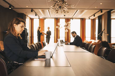 Mid adult lawyer using laptop while colleagues working in background at board room - MASF14478