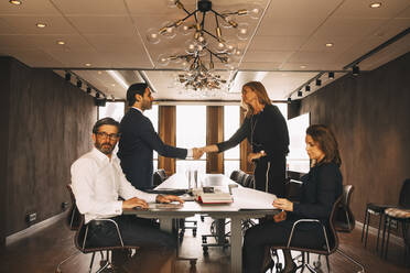 Male and female financial advisors greeting while colleagues sitting at table in law office - MASF14496