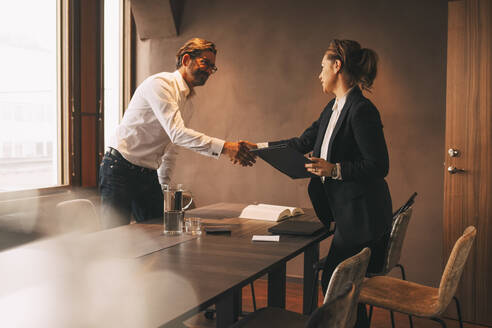 Weiblicher Anwalt schüttelt Hände mit männlichem Kunden nach einem Treffen am Tisch im Büro - MASF14516