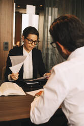Weibliche Finanzberaterin prüft Dokumente, während sie mit einem Kunden in einer Besprechung im Büro sitzt - MASF14518