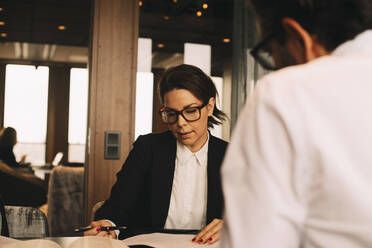 Mid adult female lawyer discussing paperwork with client at table in office - MASF14520