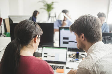 Male and female colleagues discussing over laptop on desk in creative office - MASF14539