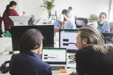 Male and female professionals discussing over laptop on desk in creative office - MASF14540