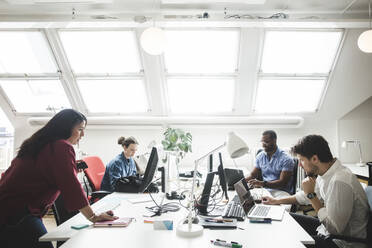 Male and female professionals using computers on desk in creative office - MASF14549