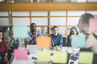 Colleagues looking at businessman explaining business plan in meeting seen through glass wall - MASF14552