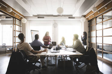 Businesswoman discussing business strategy with coworkers in meeting at board room - MASF14570