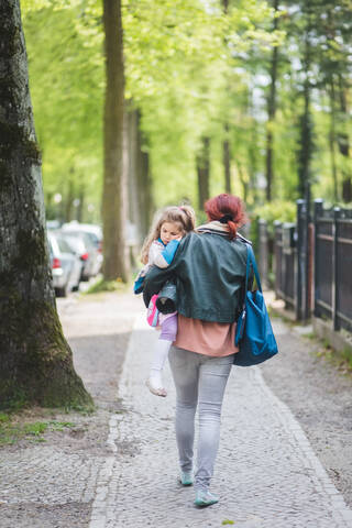 Rear view of mother carrying daughter while walking on footpath stock photo