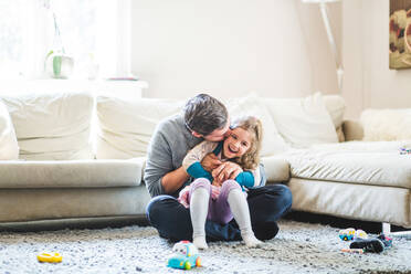 Mid adult man kissing daughter while sitting on carpet at home - MASF14592