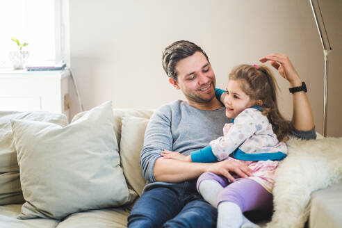 Lächelnder Vater mit Tochter, die zu Hause auf dem Sofa sitzt - MASF14594