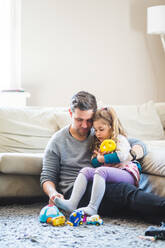 Father playing with girl while sitting on carpet in living room at home - MASF14597