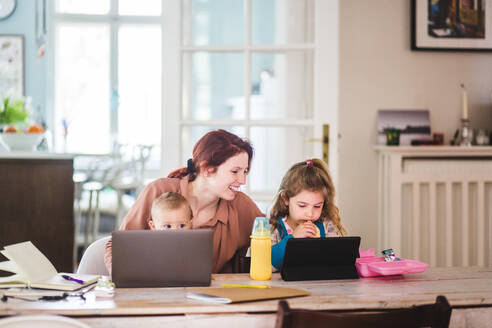 Lächelnde Frau schaut Mädchen an, die beim Essen einen Film auf einem digitalen Tablet anschauen - MASF14598