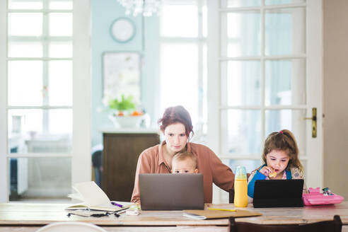 Mittlere erwachsene Frau arbeitet am Laptop, während sie mit Kindern zu Hause sitzt - MASF14599