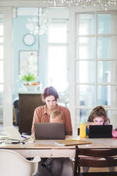 Frau arbeitet am Laptop und sitzt mit Kindern am Tisch - MASF14600