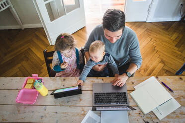 Hoher Blickwinkel des Mannes, der einen Laptop benutzt, während er mit seinem süßen Sohn bei seiner Tochter sitzt und auf ein digitales Tablet schaut - MASF14601